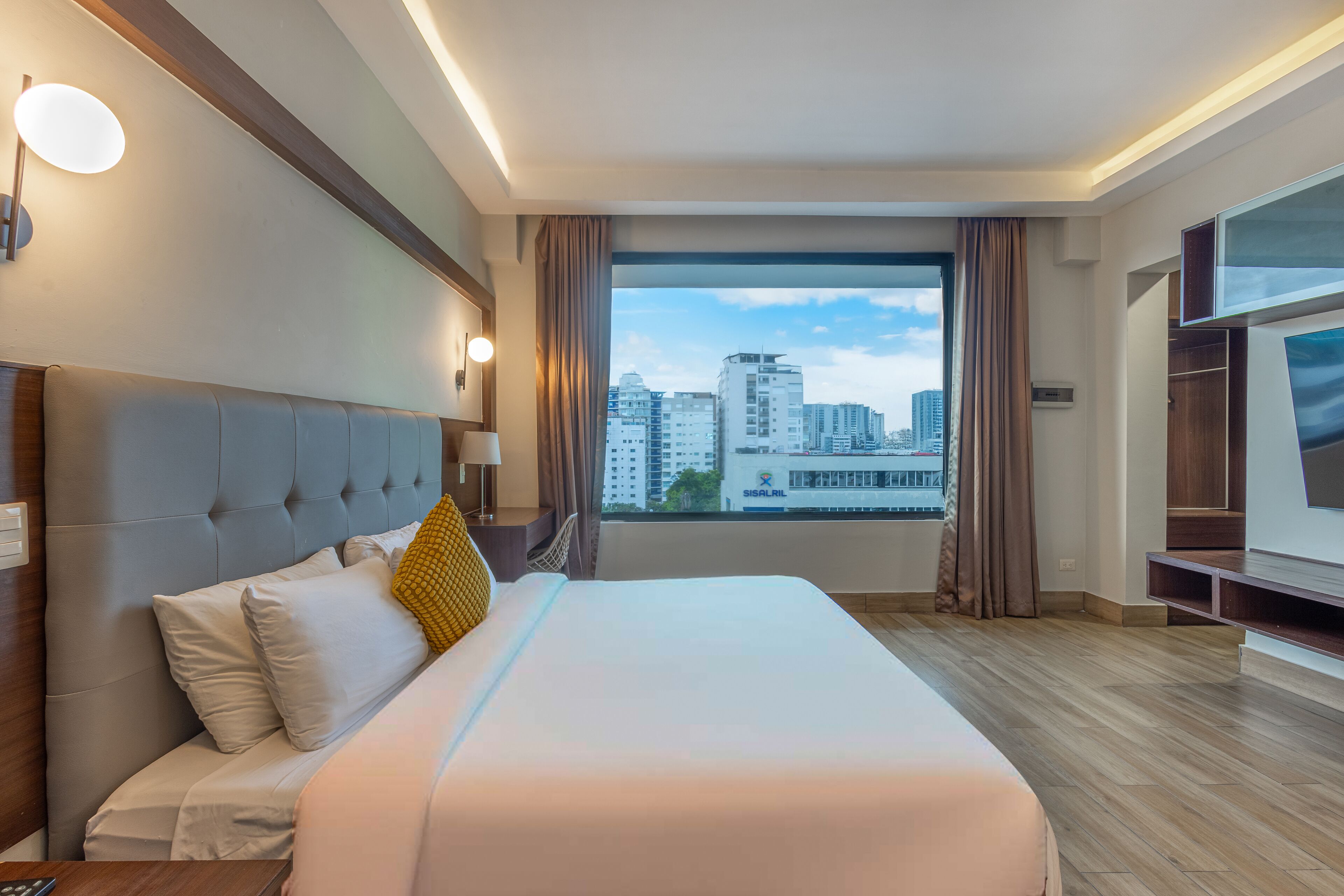 Een hotelkamer met een groot bed, een televisie, uitzicht over de stad en een modern design.