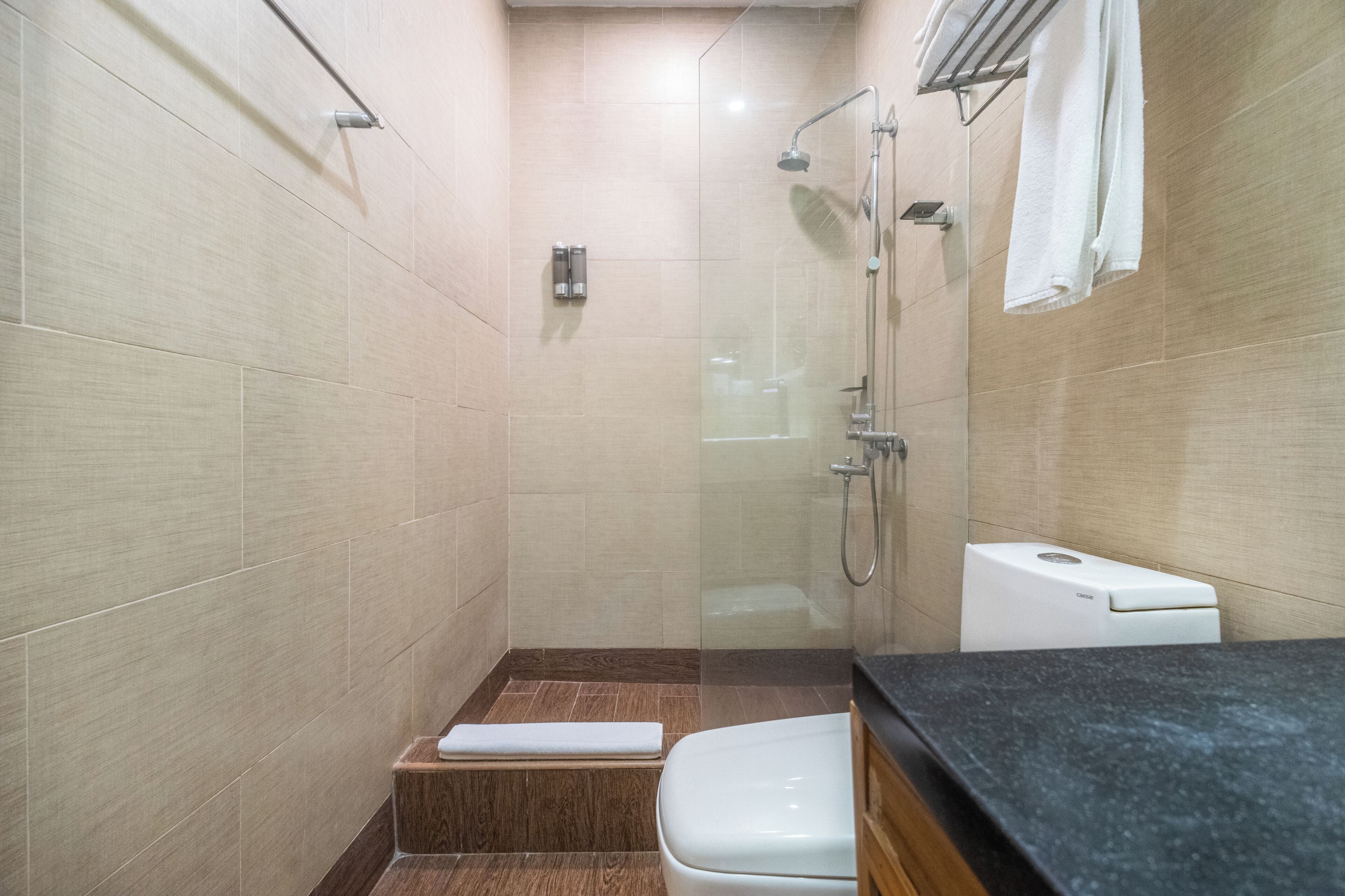 Un baño moderno con ducha de vidrio, inodoro blanco y un escalón de madera que lleva a la ducha.