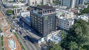 Un edificio de varios pisos con terraza en la azotea, rodeado de otros edificios y una calle concurrida.