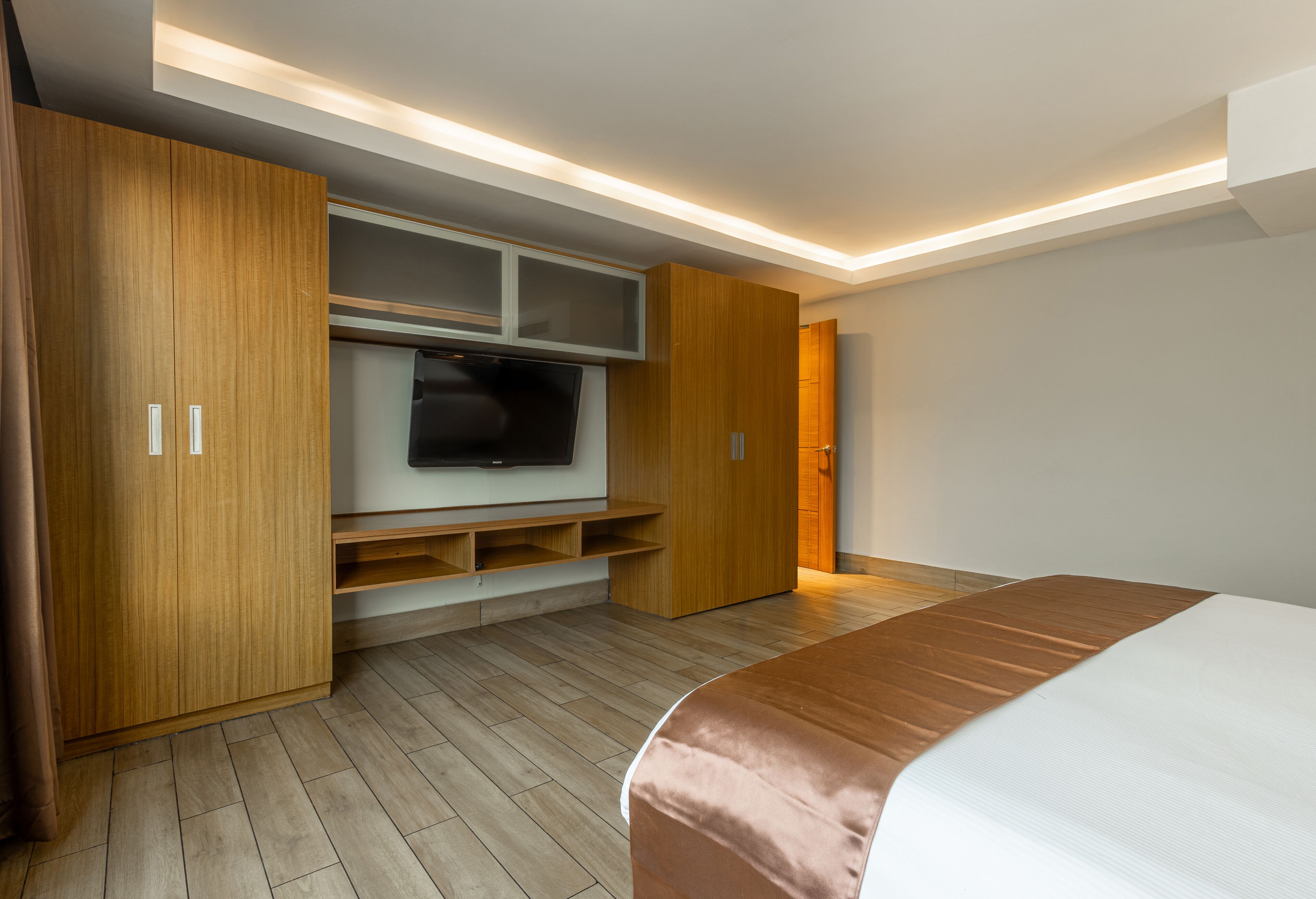 Un dormitorio moderno con una cama grande, armario de madera, televisor integrado y luces empotradas.