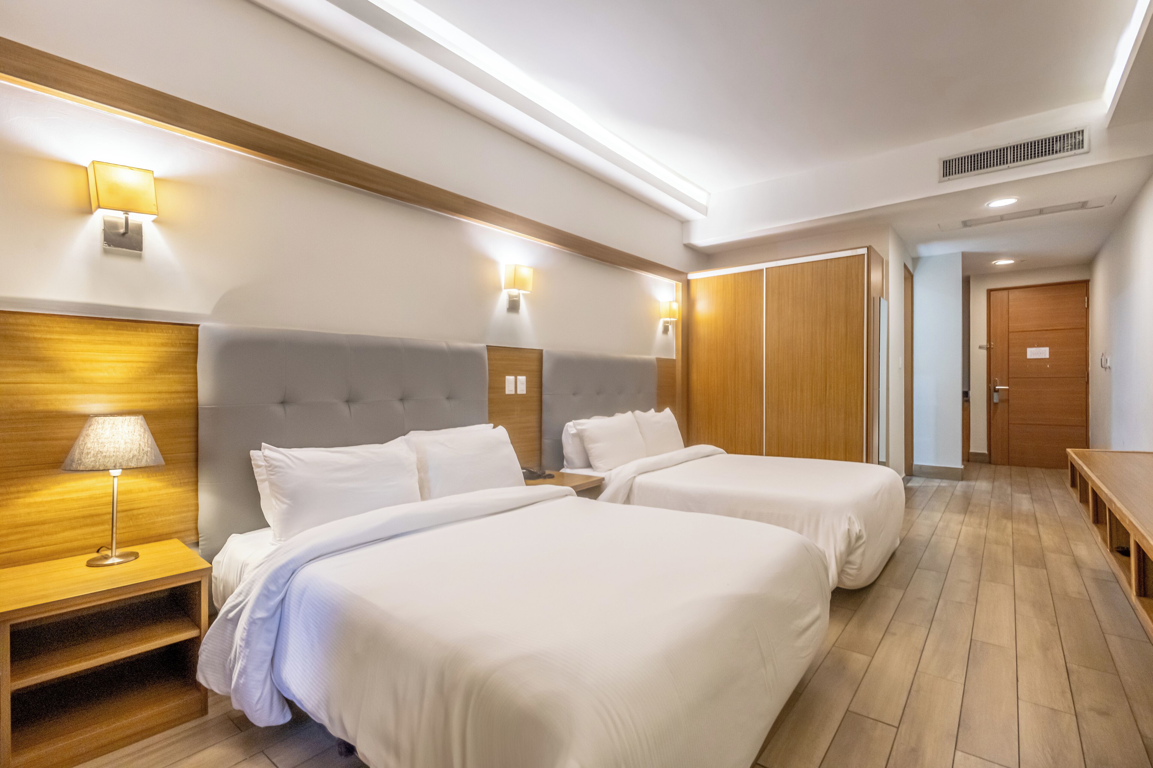 Une chambre d’hôtel avec deux lits, une tête de lit en bois, des lampes de chevet et un banc en bois.