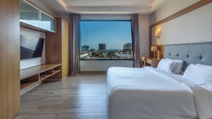 Een moderne hotelkamer met een groot bed, een televisie op een houten standaard, uitzicht over de stad en een balkon.