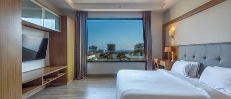 A modern hotel room with a large bed, a TV on a wooden stand, a city view, and a balcony.