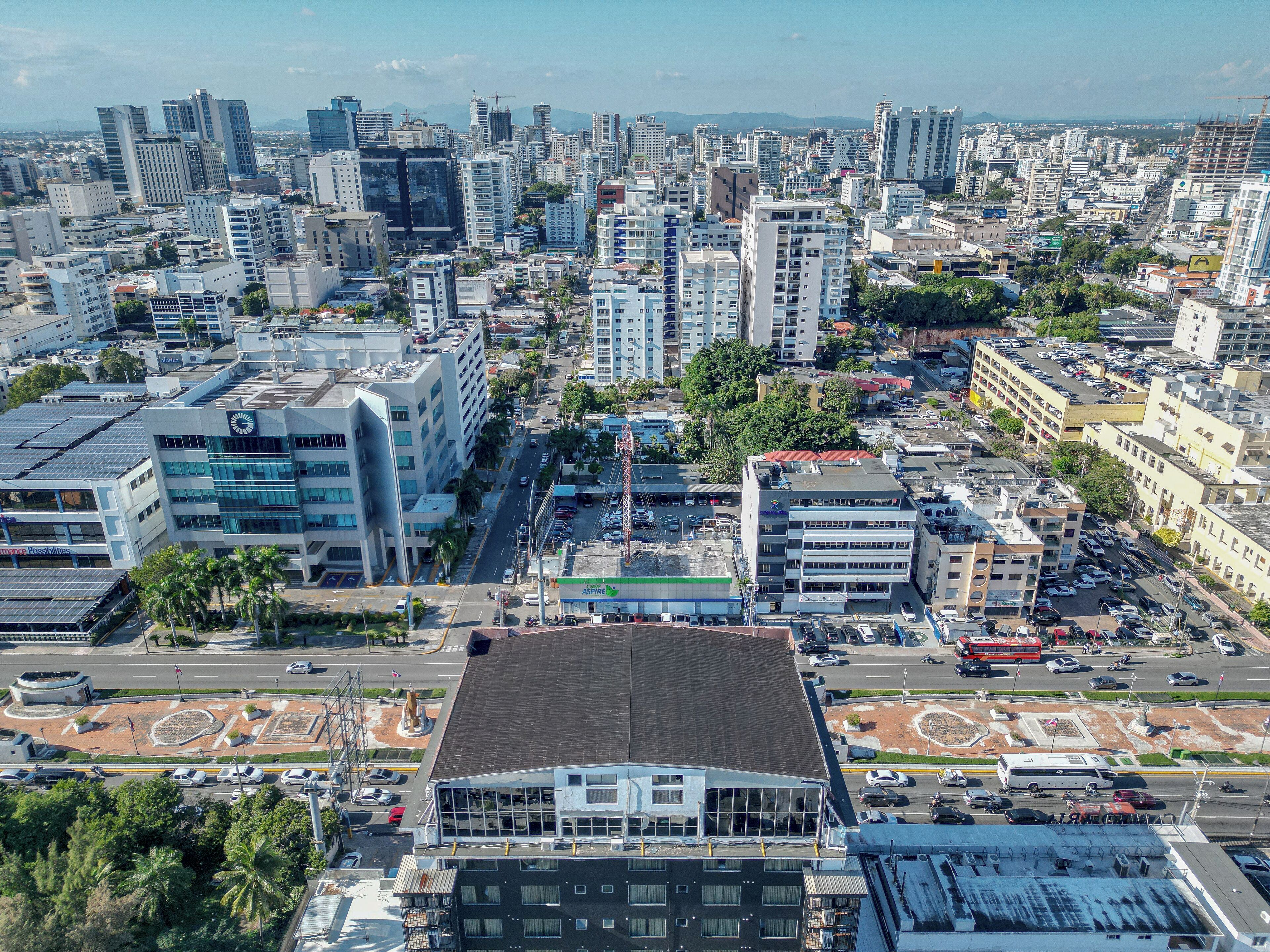 Un paisaje urbano con edificios modernos, una avenida central y un estacionamiento.