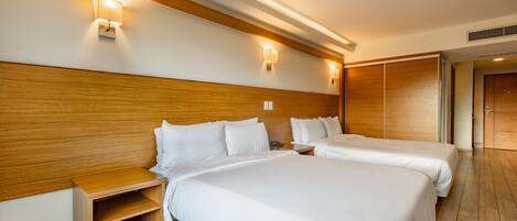 Una habitación de hotel con dos camas, cabecero de madera, mesitas de noche e iluminación empotrada.