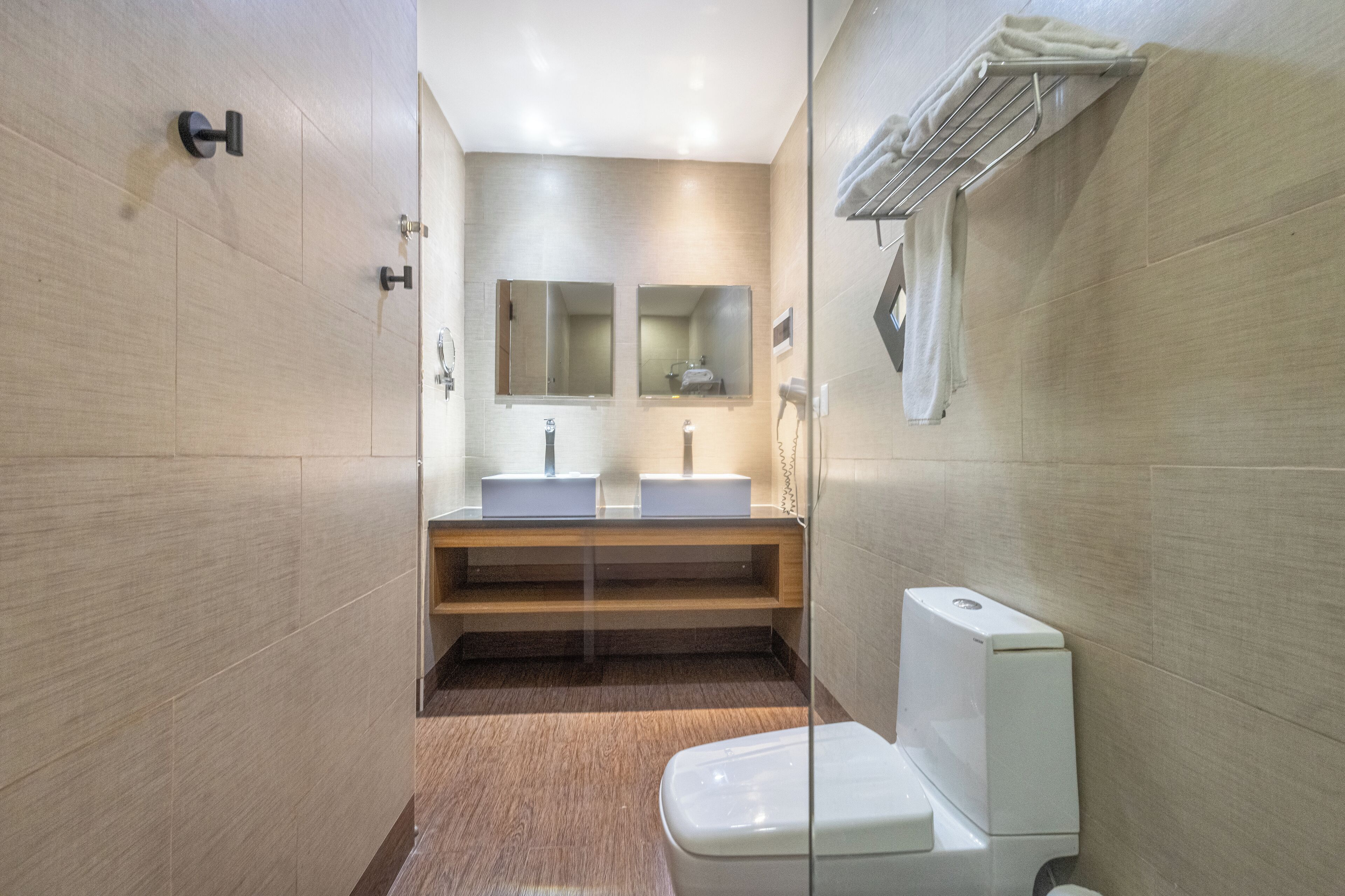 A modern bathroom with two sinks, a mirror, and a toilet.