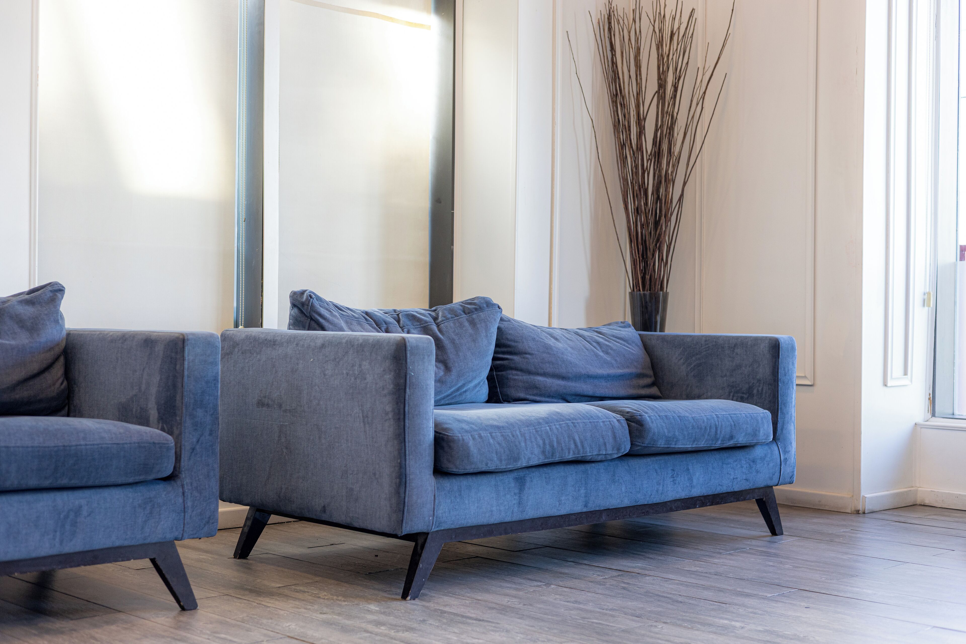 A modern living room with two grey sofas and a tall vase of branches.