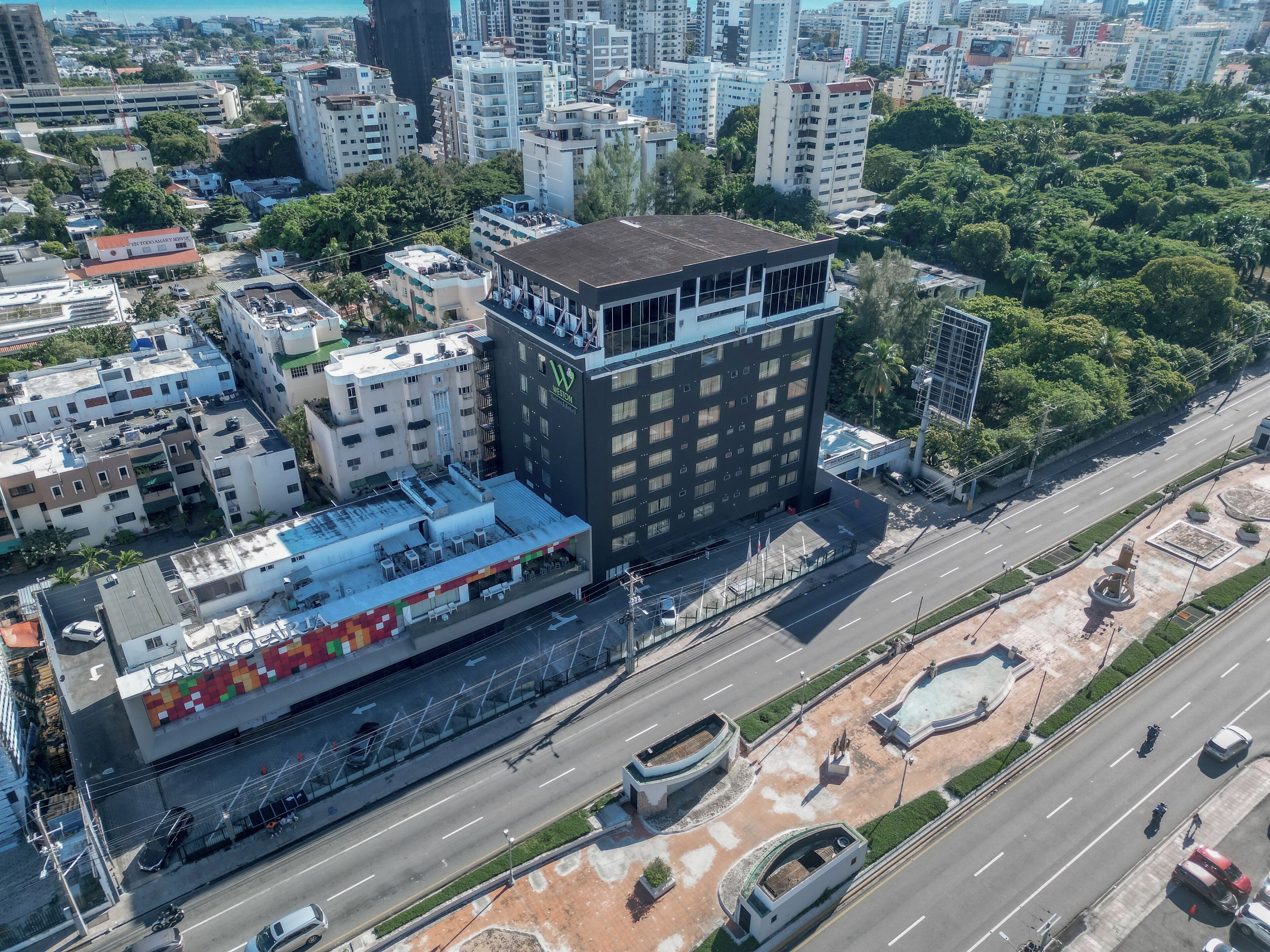 Une vue aérienne d’une ville, avec un bâtiment imposant doté d’une terrasse sur le toit et d’un parking.