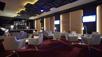 Un espace lounge moderne avec des chaises blanches, une moquette rouge et un bar en arrière-plan.