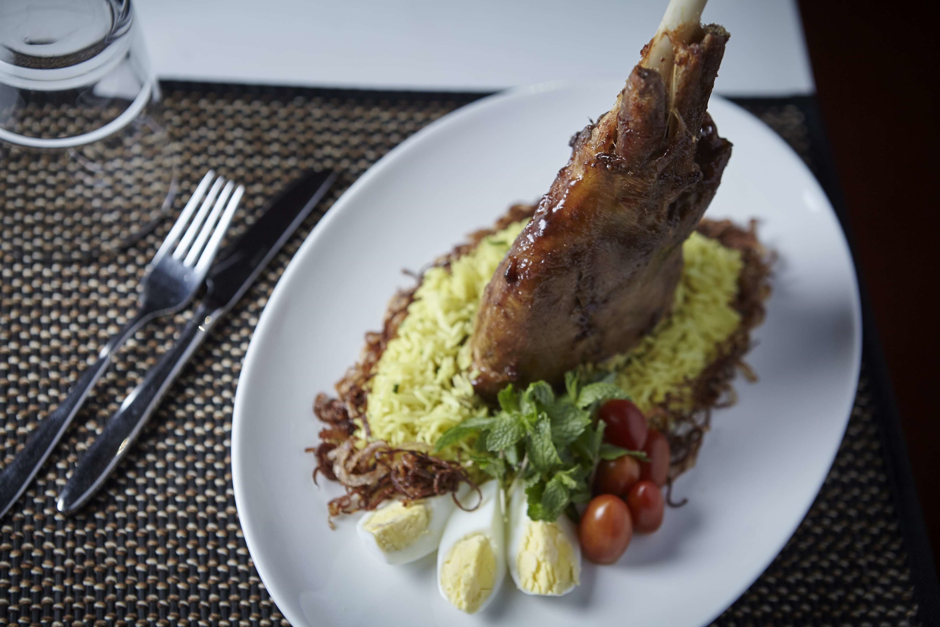 A plate with a lamb shank, rice, and vegetables.