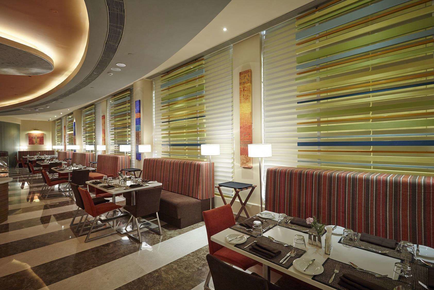 En moderne hotellobby med stribede vinduespersienner, et centralt siddeområde med borde og stole, og en slebet marmorgulv.