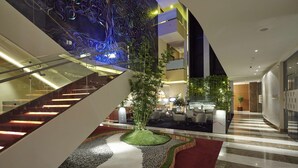 Un moderno vestíbulo de hotel con una escalera central, un jardín decorativo y una zona de estar con un letrero que dice 'mista'.