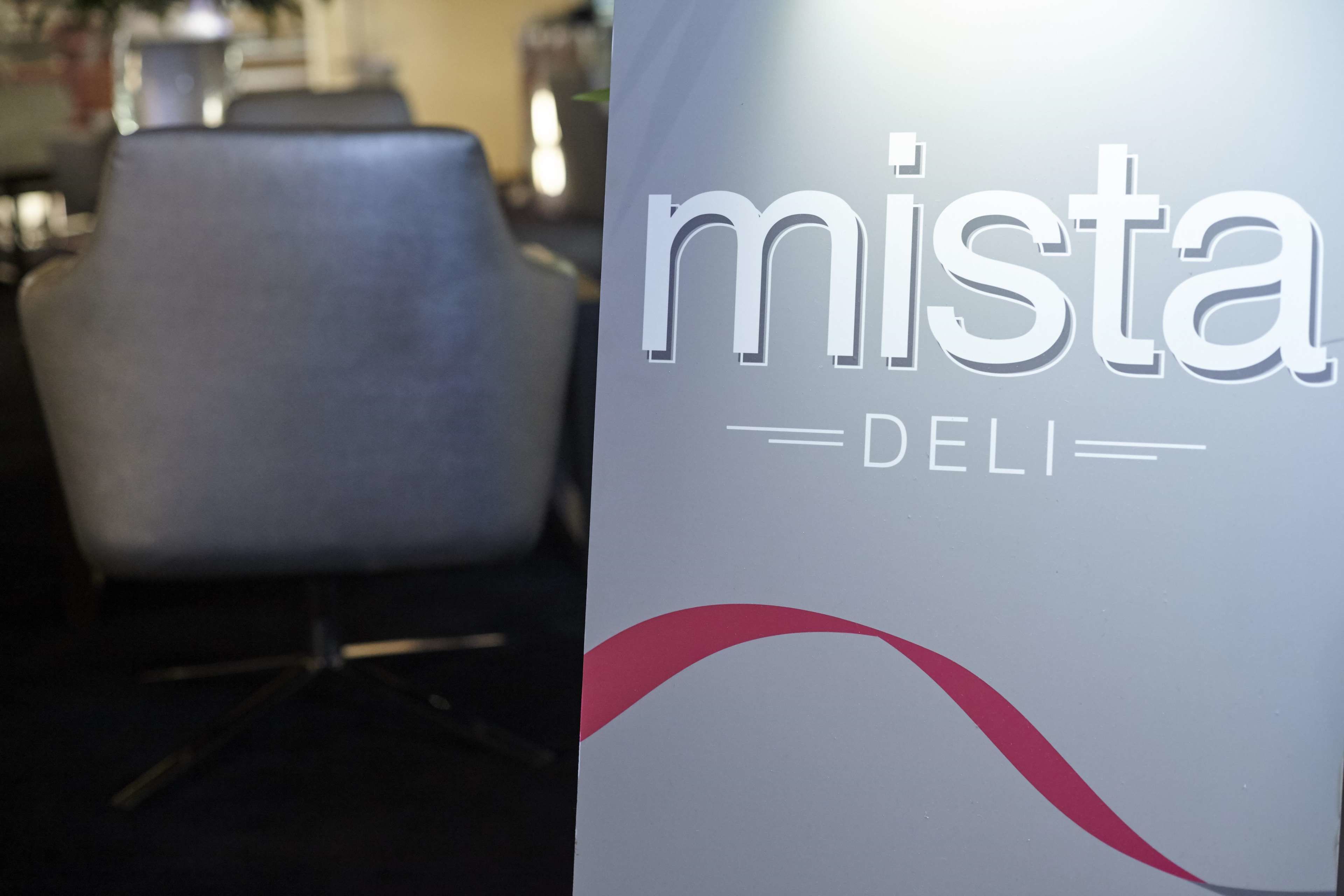 A sign with the text "mista DELI" and a partial view of a modern office chair.
