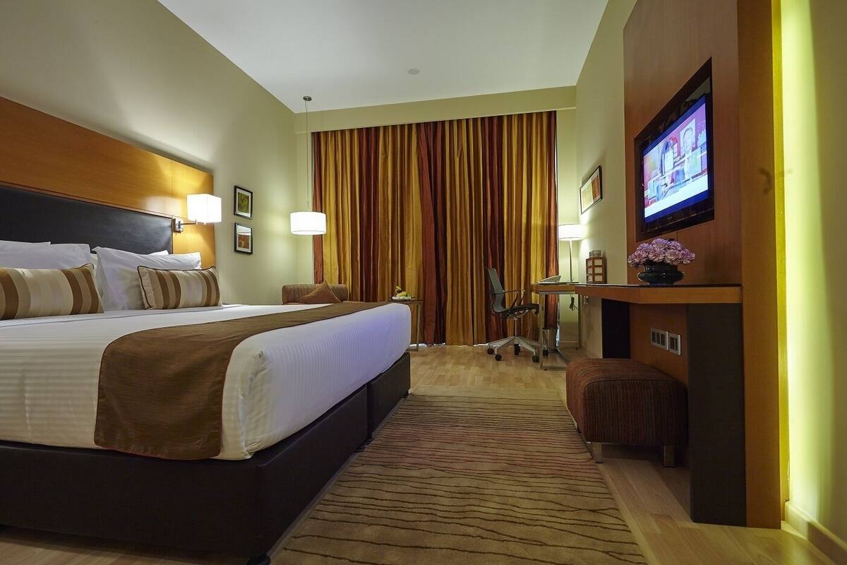 Ein Hotelzimmer mit einem großen Bett, einem Schreibtisch, einem Sessel, einem Fernseher und einem Vorhang.