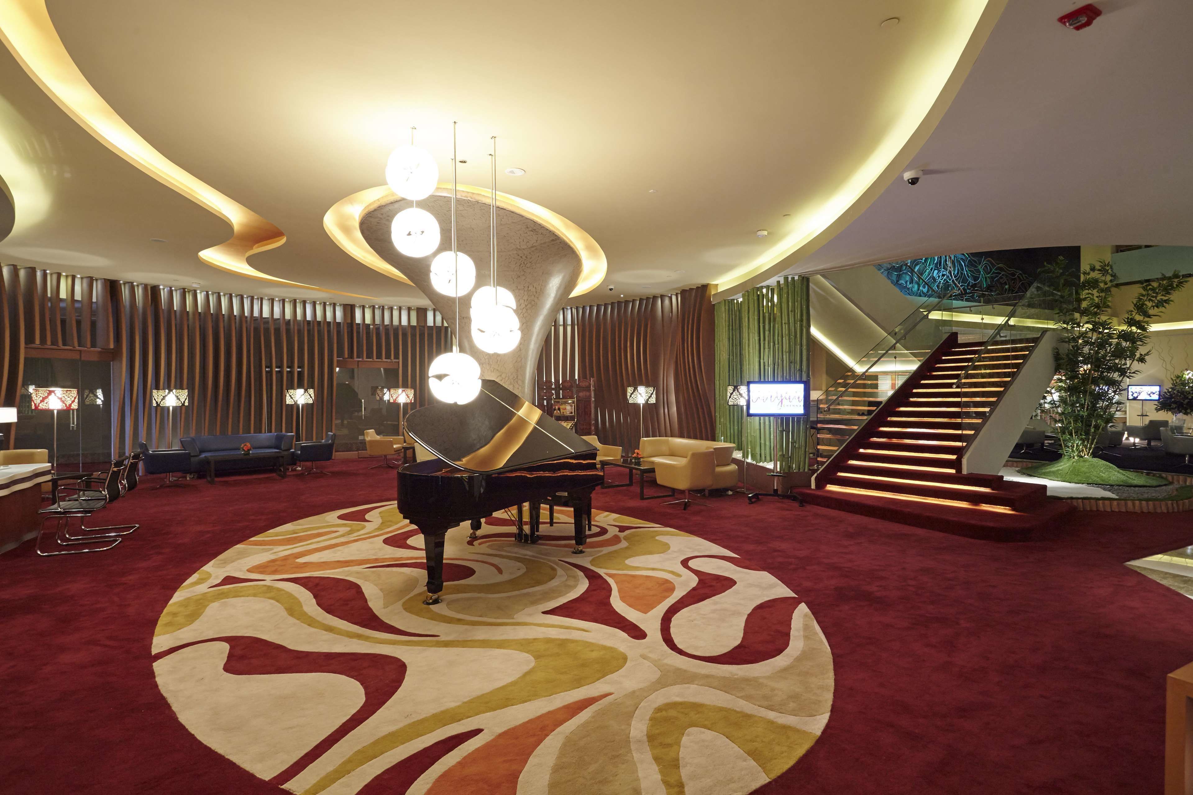 A grand lobby with a grand piano, a large circular carpet, and a staircase with a glass railing.