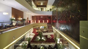 Un hall de hotel de varios niveles con un atrio central, una escalera y un gran mural abstracto.