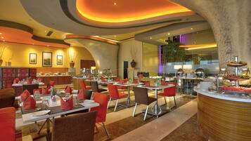 Un restaurante moderno con varias mesas y sillas, una zona de buffet y un espejo grande que refleja el interior.