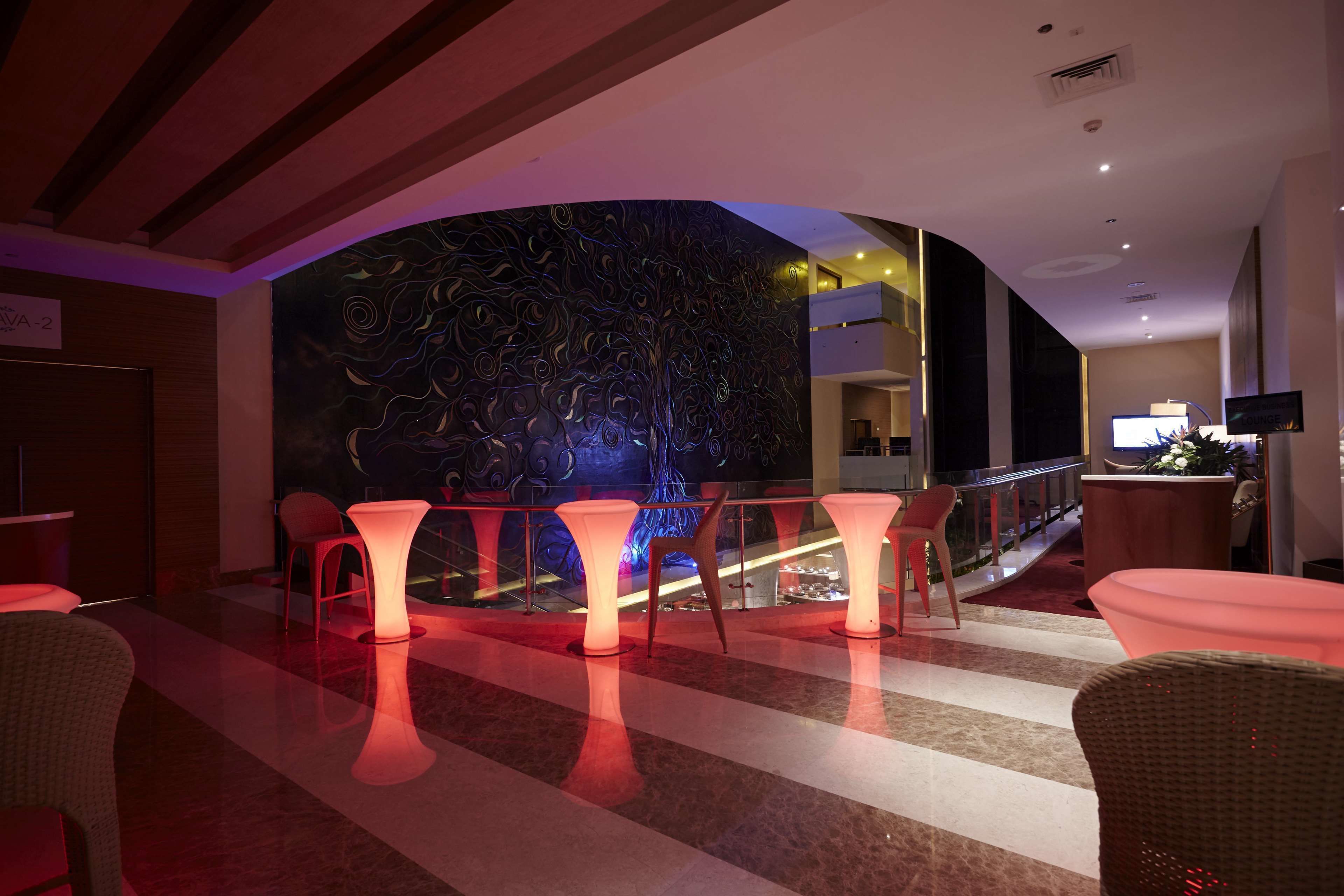 A modern lobby with a curved wall featuring an abstract mural, illuminated seating areas, and a visible staircase leading to an upper level.