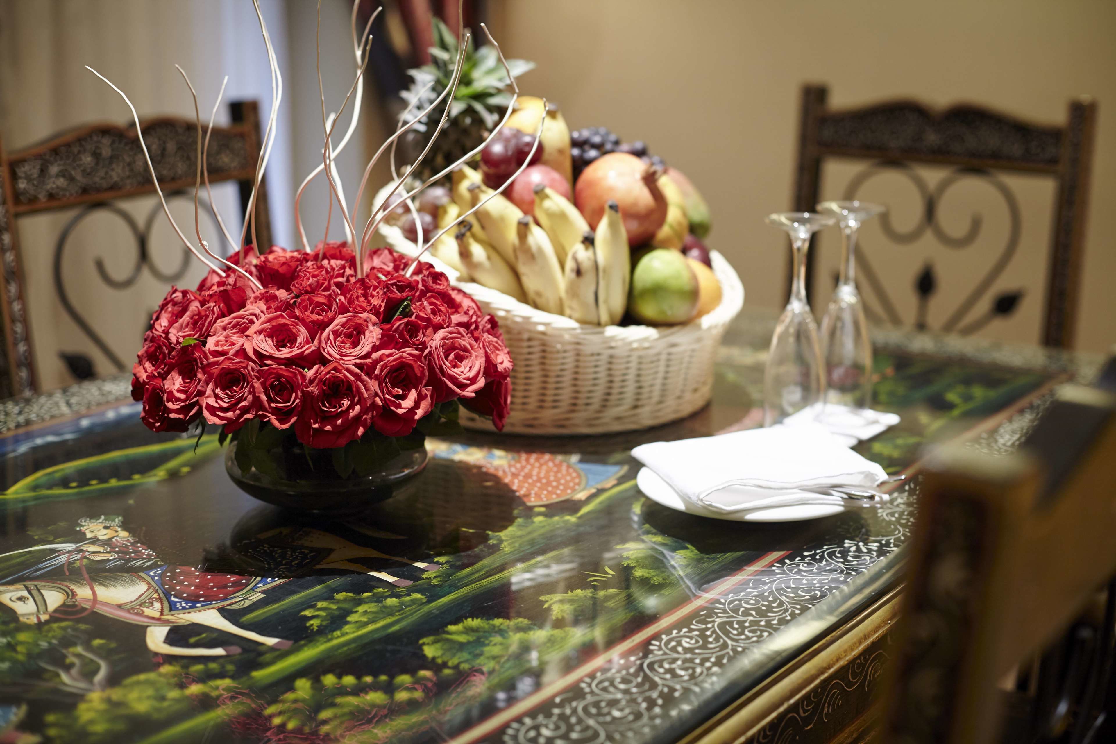 A dining table with a floral centerpiece, a fruit basket, and a clear glass vase.