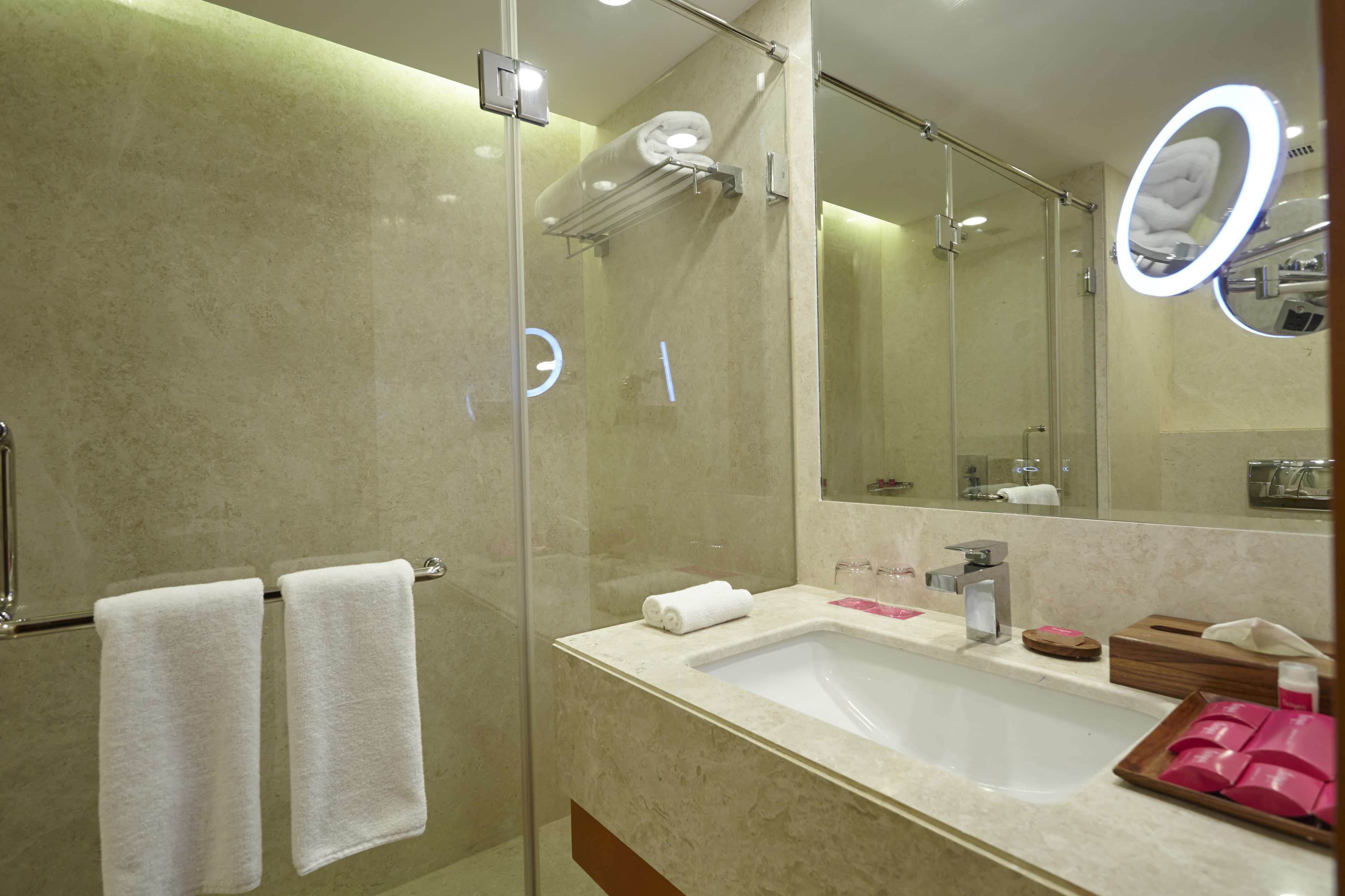 Un baño moderno con ducha envuelta en vidrio, un espejo grande y un lavamanos con artículos de aseo.