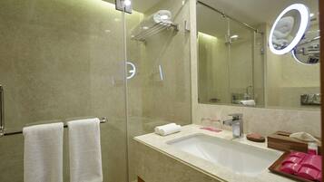 Un baño moderno con ducha envuelta en vidrio, un espejo grande y un lavamanos con artículos de aseo.
