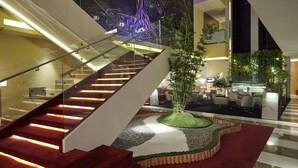 Un moderno vestíbulo de hotel con una escalera de cristal, plantas de interior y una zona de estar.