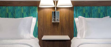 A hotel room with two beds, a wooden headboard, a nightstand, and a wall-mounted lamp.