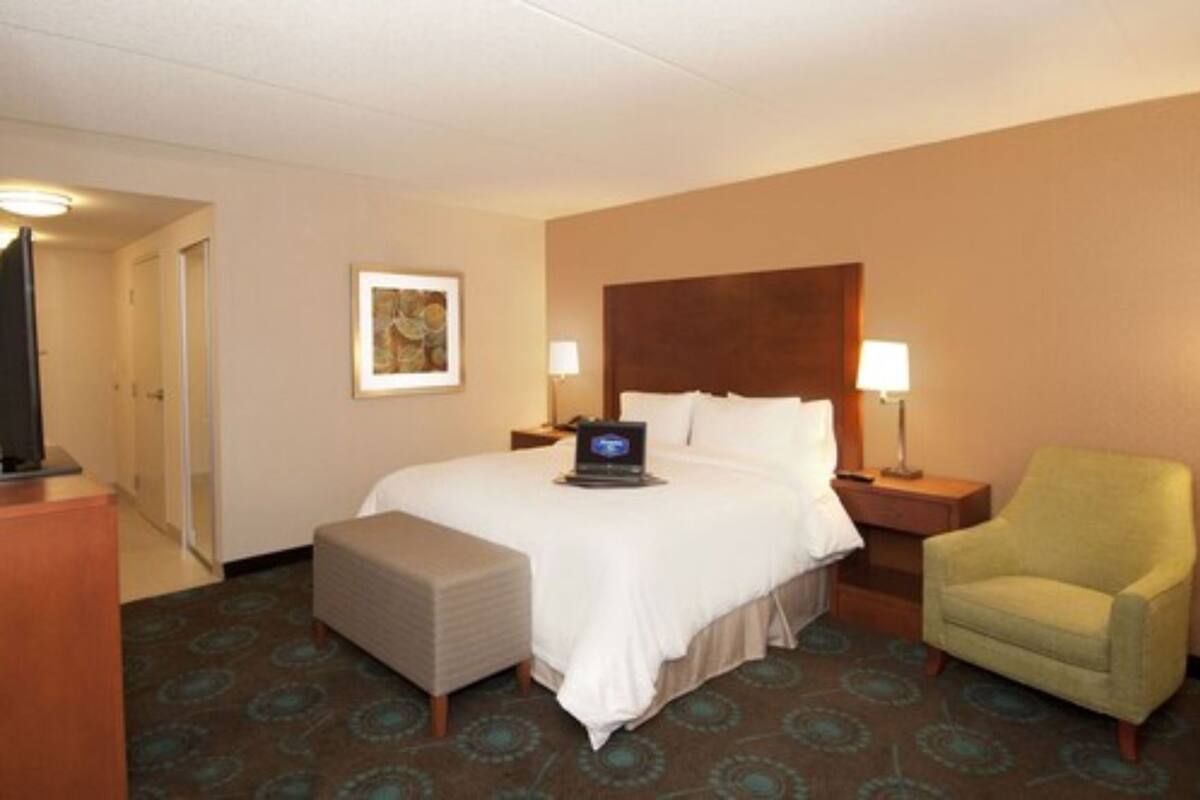 A hotel room with a bed, a desk, a chair, a television, a lamp, and a patterned carpet.