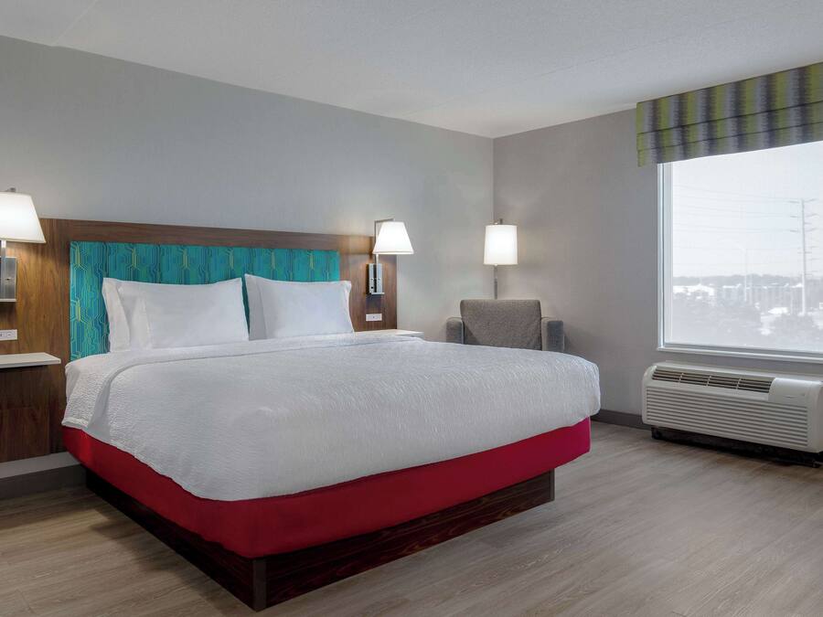 Habitación de hotel con una cama grande, dos lámparas de noche, una ventana con vistas y aire acondicionado instalado en la pared.