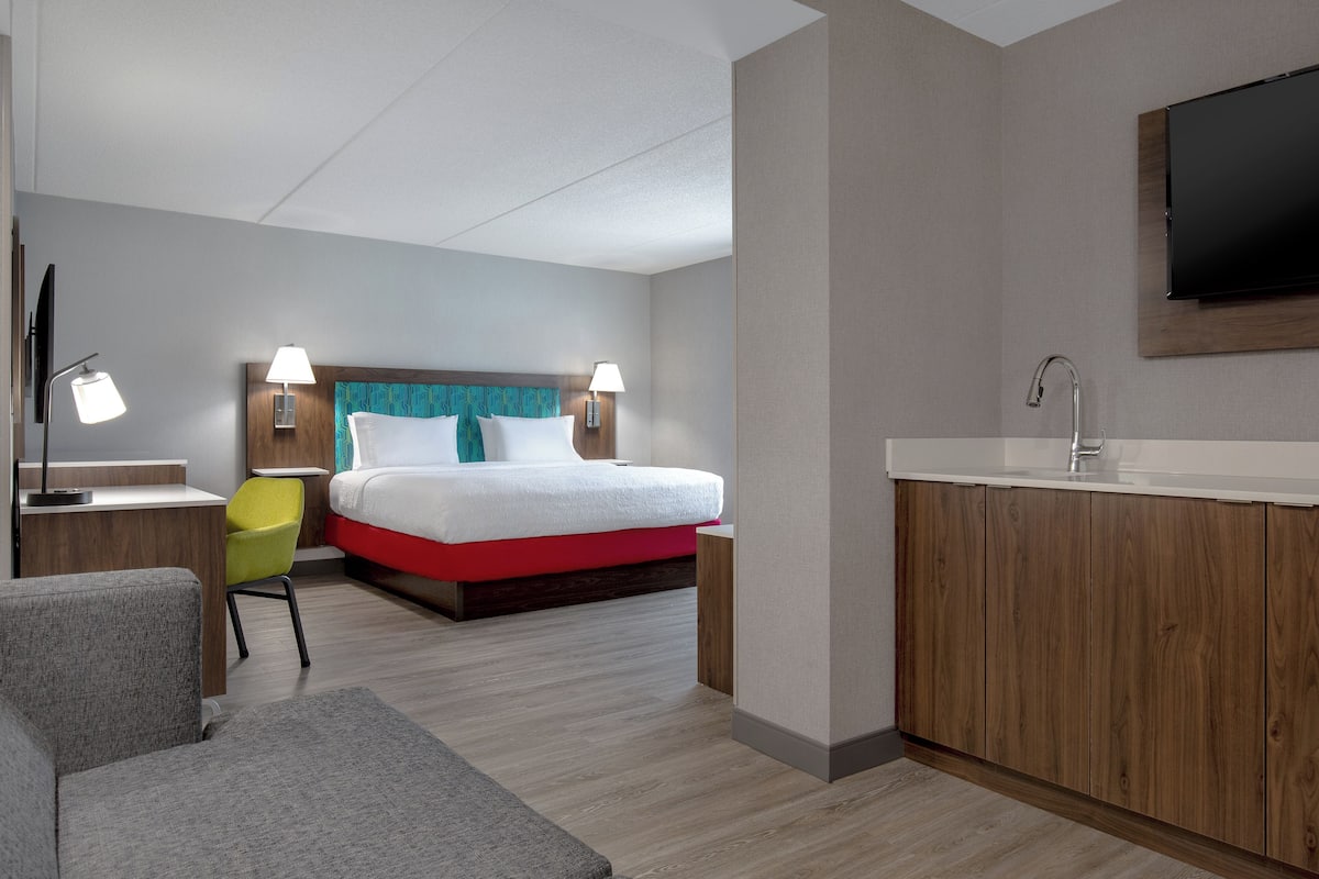 Moderni hotellihuone, jossa on sänky, työpöytä, tuoli, televisio ja kylpyhuone.