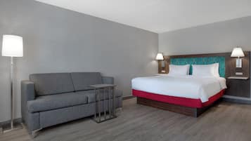 A hotel room with a grey sofa, a small table, a bed with a red base, and two bedside lamps.