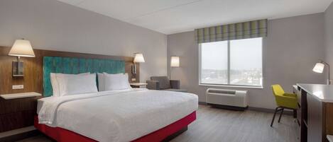 Habitación de hotel con una cama grande, un escritorio, una silla y una ventana con vista a la ciudad.