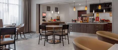 A modern hotel lobby with a dining area, a kitchen, and a seating area.