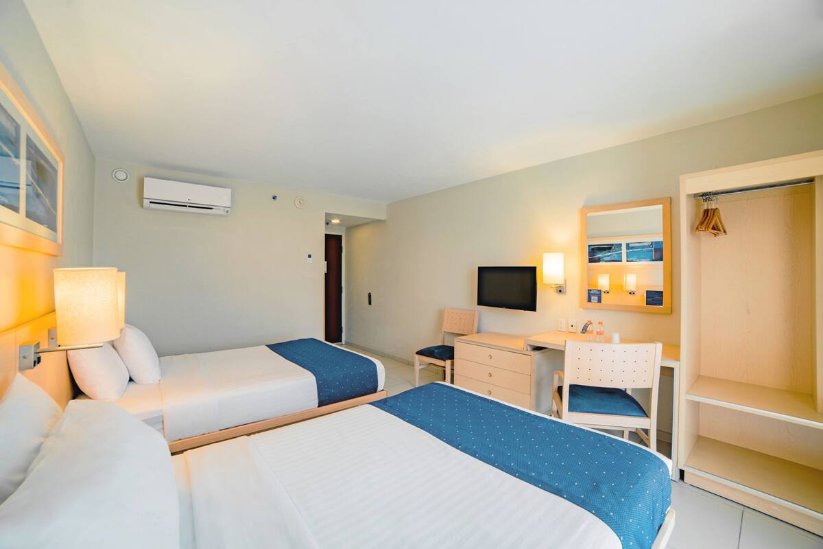 Ein Hotelzimmer mit zwei Betten, einem Schreibtisch, einem Stuhl, einem Fernseher, einem Spiegel und einem Kleiderschrank.