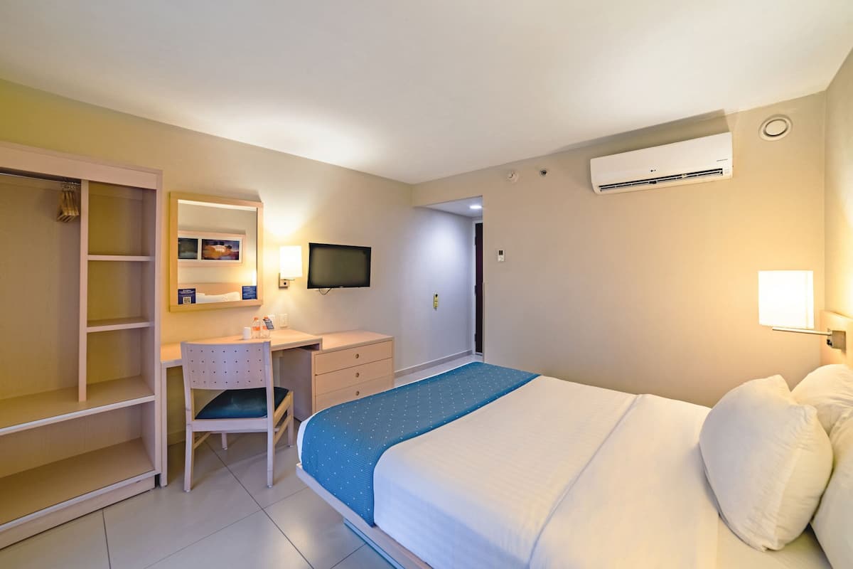 Ein Hotelzimmer mit Bett, Schreibtisch, Stuhl, Kleiderschrank, Fernseher und Klimaanlage.