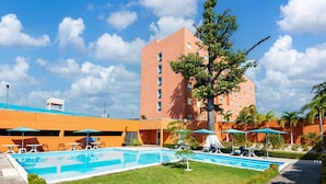 Un patio de hotel con piscina, mobiliario exterior y un edificio alto al fondo.