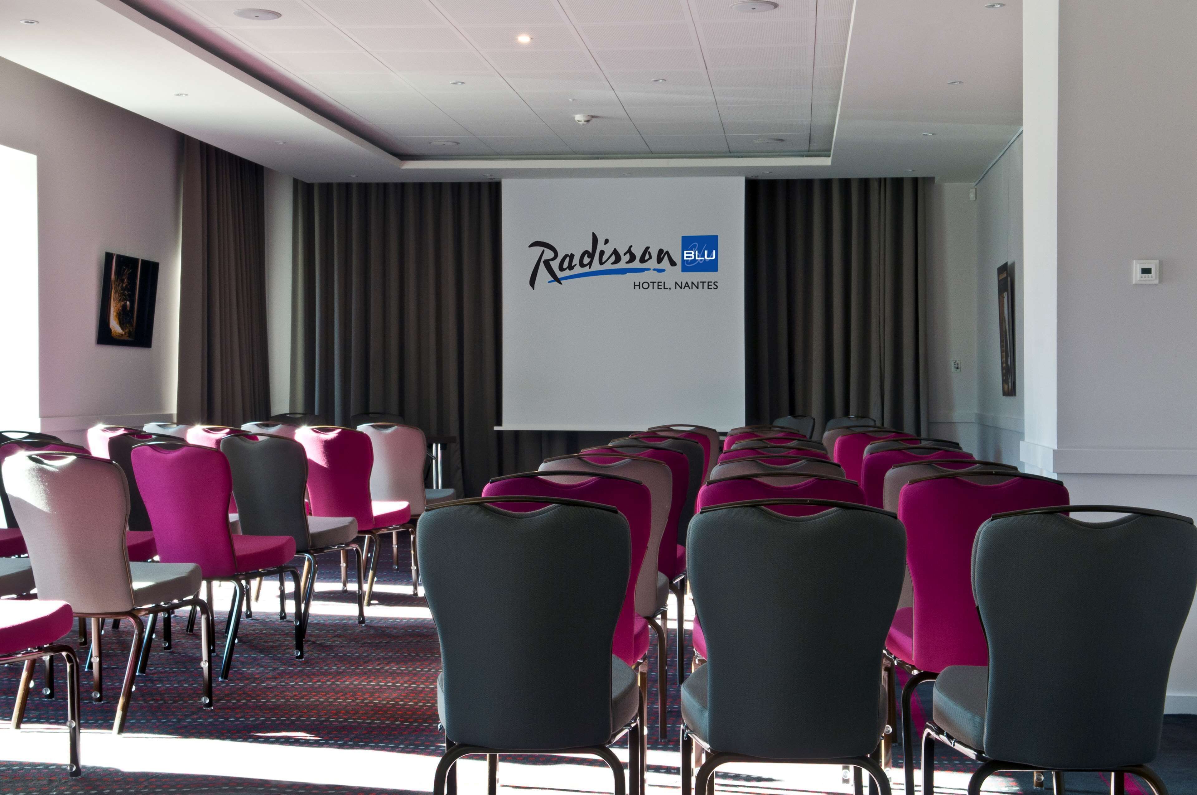 A conference room with rows of chairs, a projection screen, and a Radisson Blu Hotel sign.