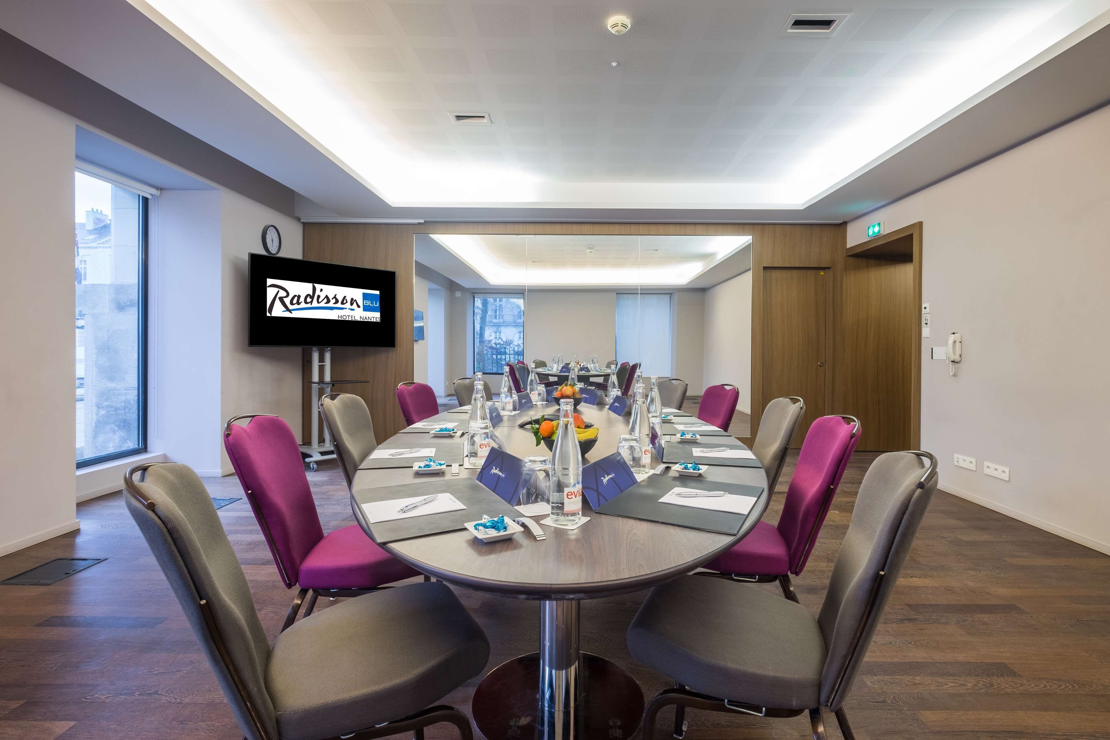 Un salón de conferencias con una mesa redonda, sillas y una pantalla de televisión mostrando el nombre del Hotel Radisson.