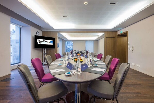 Un salón de conferencias con una mesa redonda, sillas y una pantalla de televisión mostrando el nombre del Hotel Radisson.