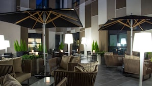 A modern outdoor seating area with wicker furniture, black umbrellas, and ambient lighting. - Radisson Blu Hotel Nantes (Nantes)