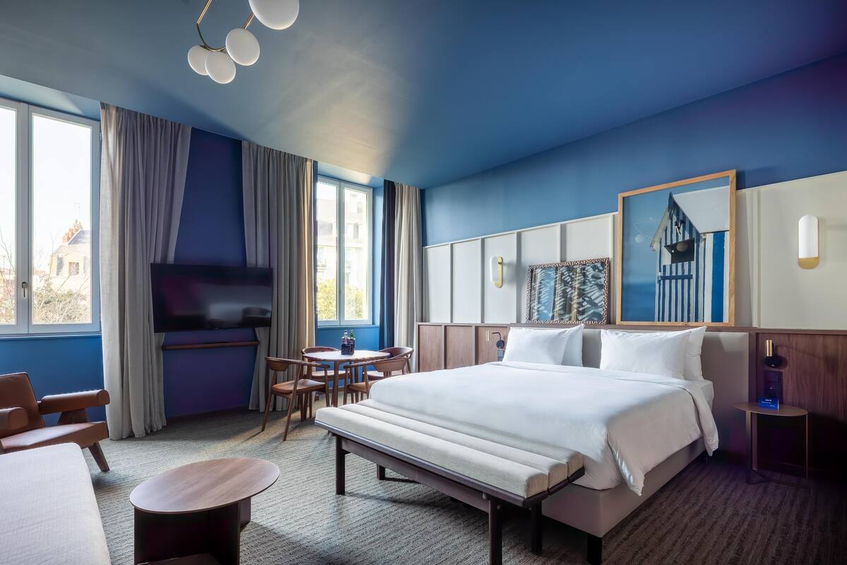 Habitación de hotel con una cama grande, un escritorio, una silla, un televisor y una ventana con cortinas.
