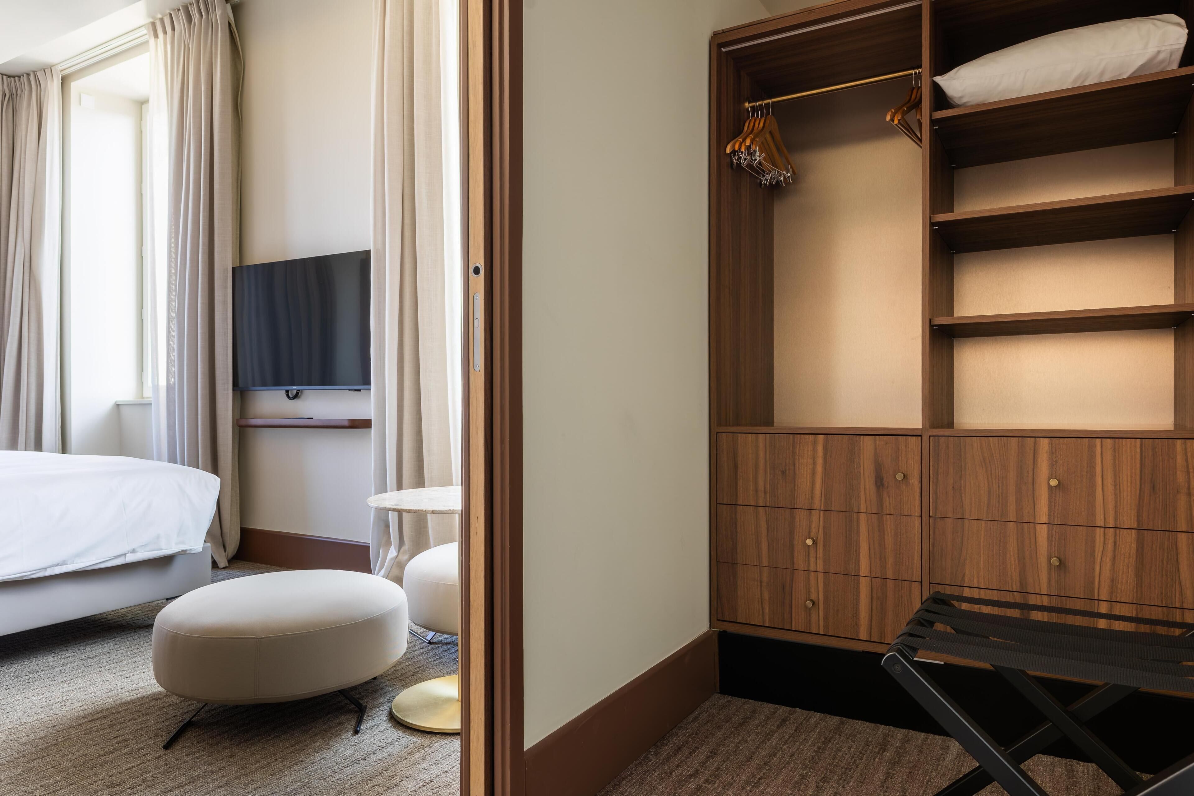 Una habitación de hotel con una cama, un televisor montado en la pared, un armario de madera y una mesita.