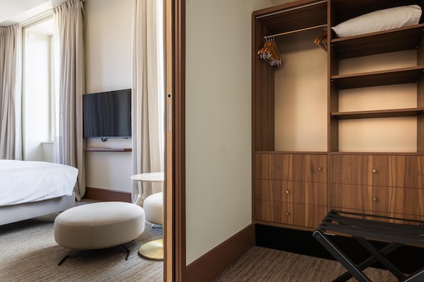 A hotel room with a bed, a TV mounted on the wall, a wooden wardrobe, and a small table.