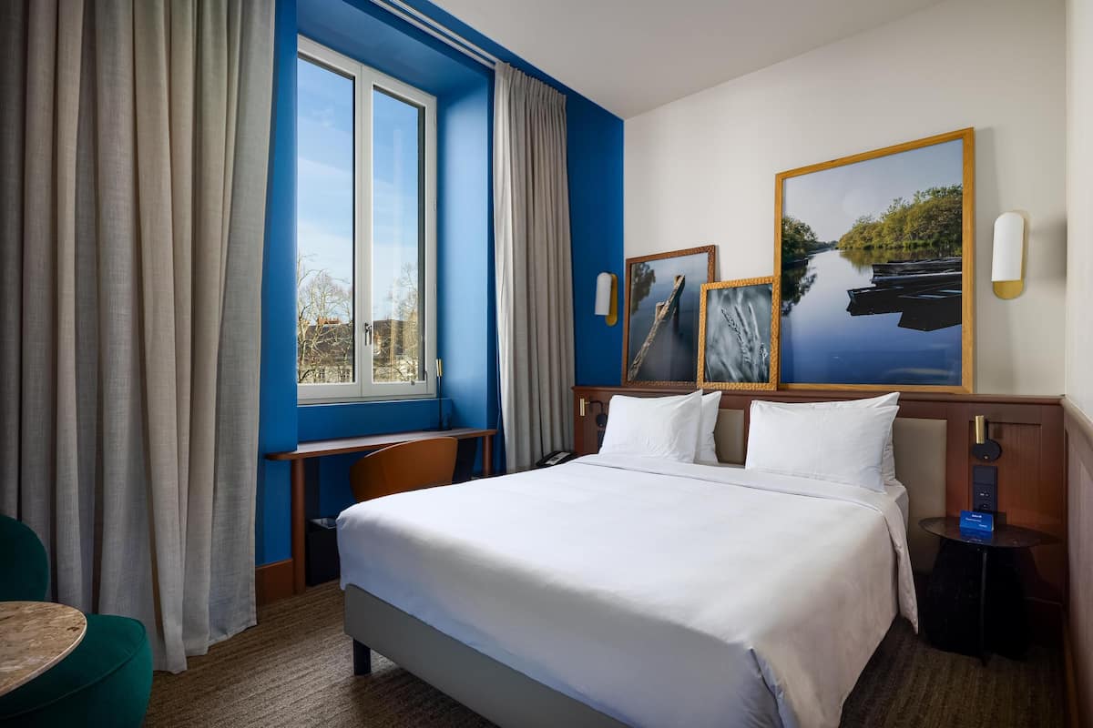 Una habitación de hotel con una cama grande, un escritorio, una silla, una mesita y una ventana con cortinas.