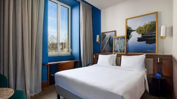 A hotel room with a large bed, a desk, a chair, a small table, and a window with curtains.