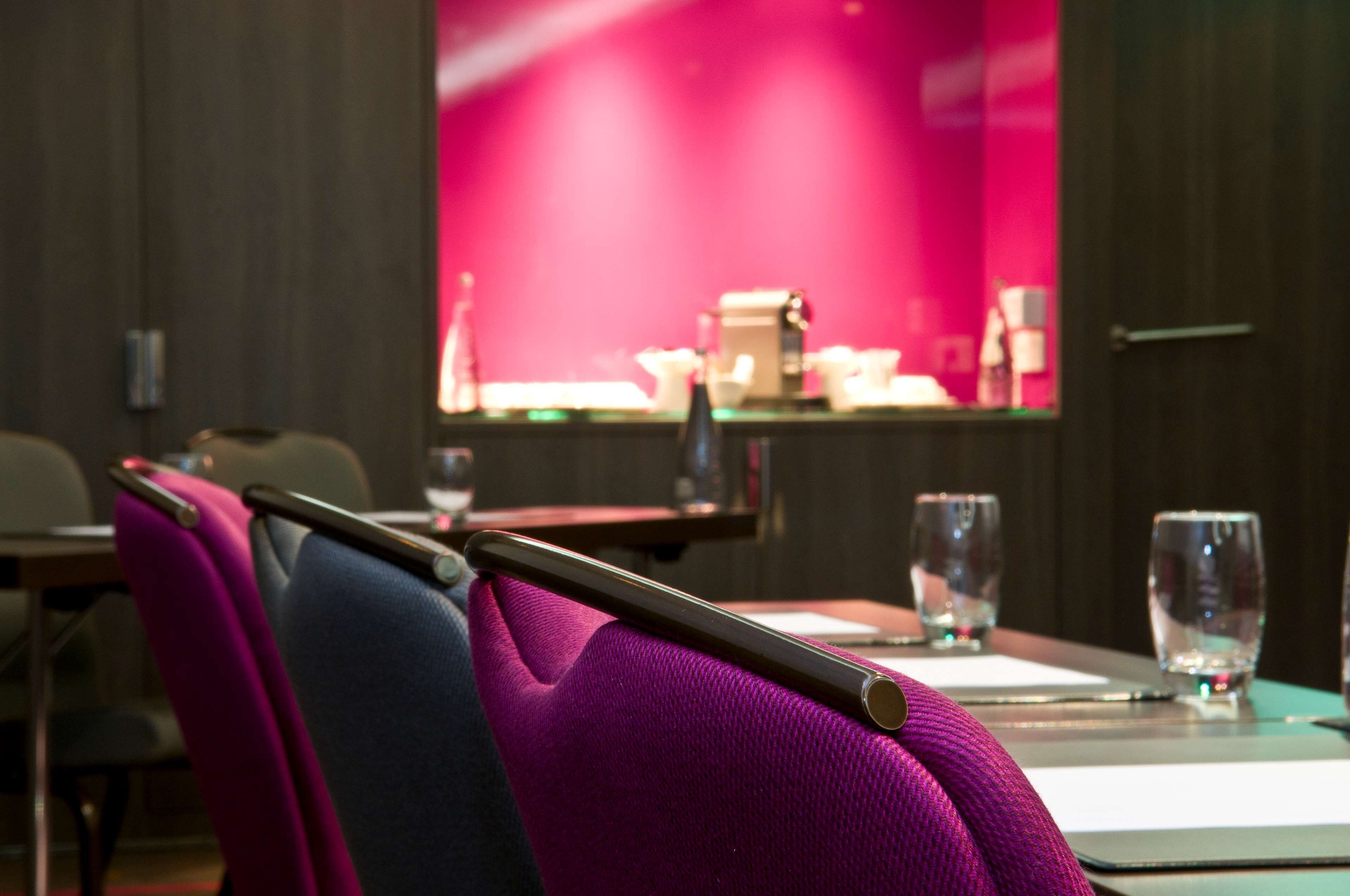 Un salón de conferencias con una mesa lista para una reunión, sillas y vistas a un área de bar.