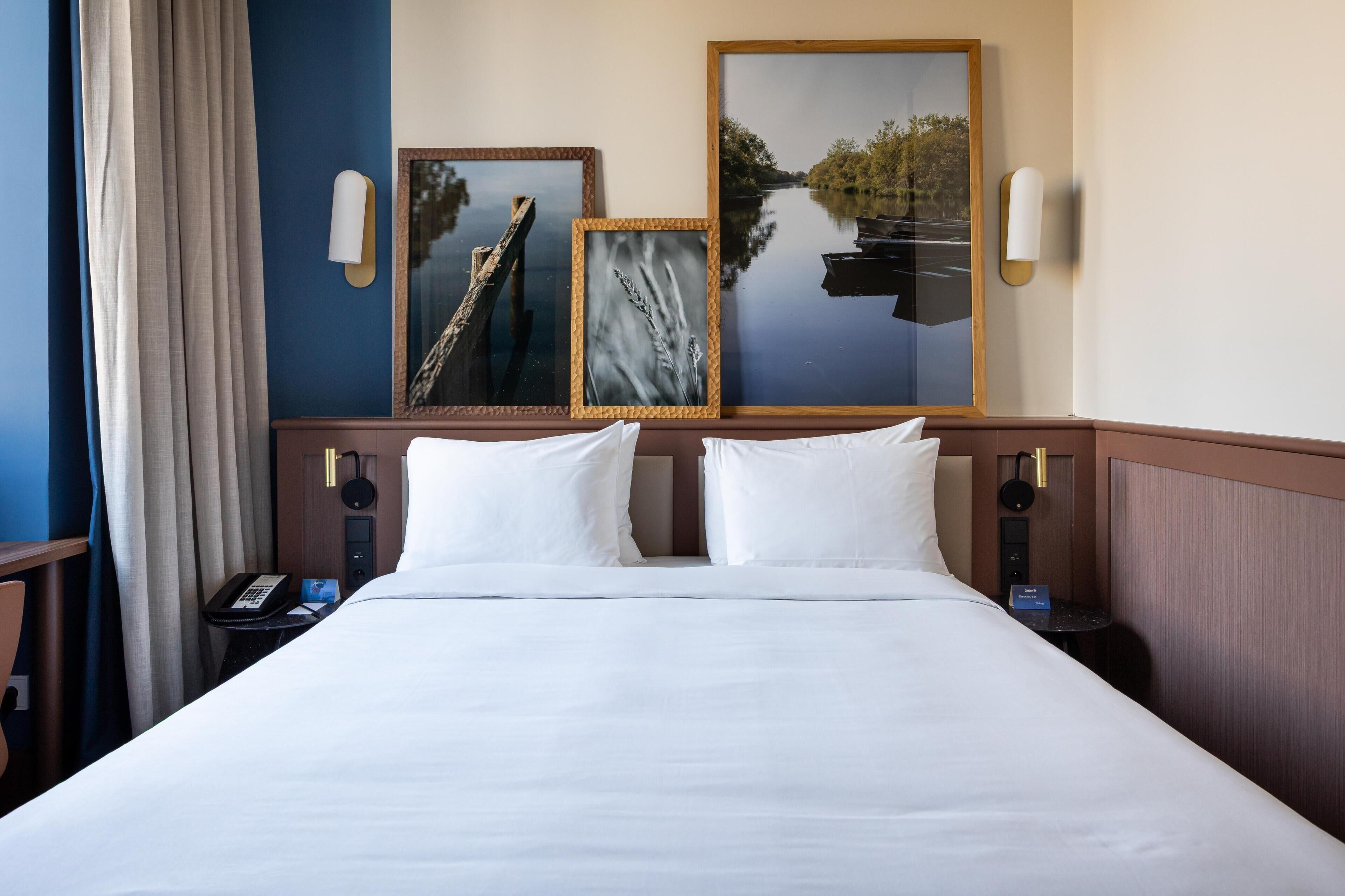 Hotelkamer met een groot bed, twee nachtkastjes, een telefoon en wandlampen.