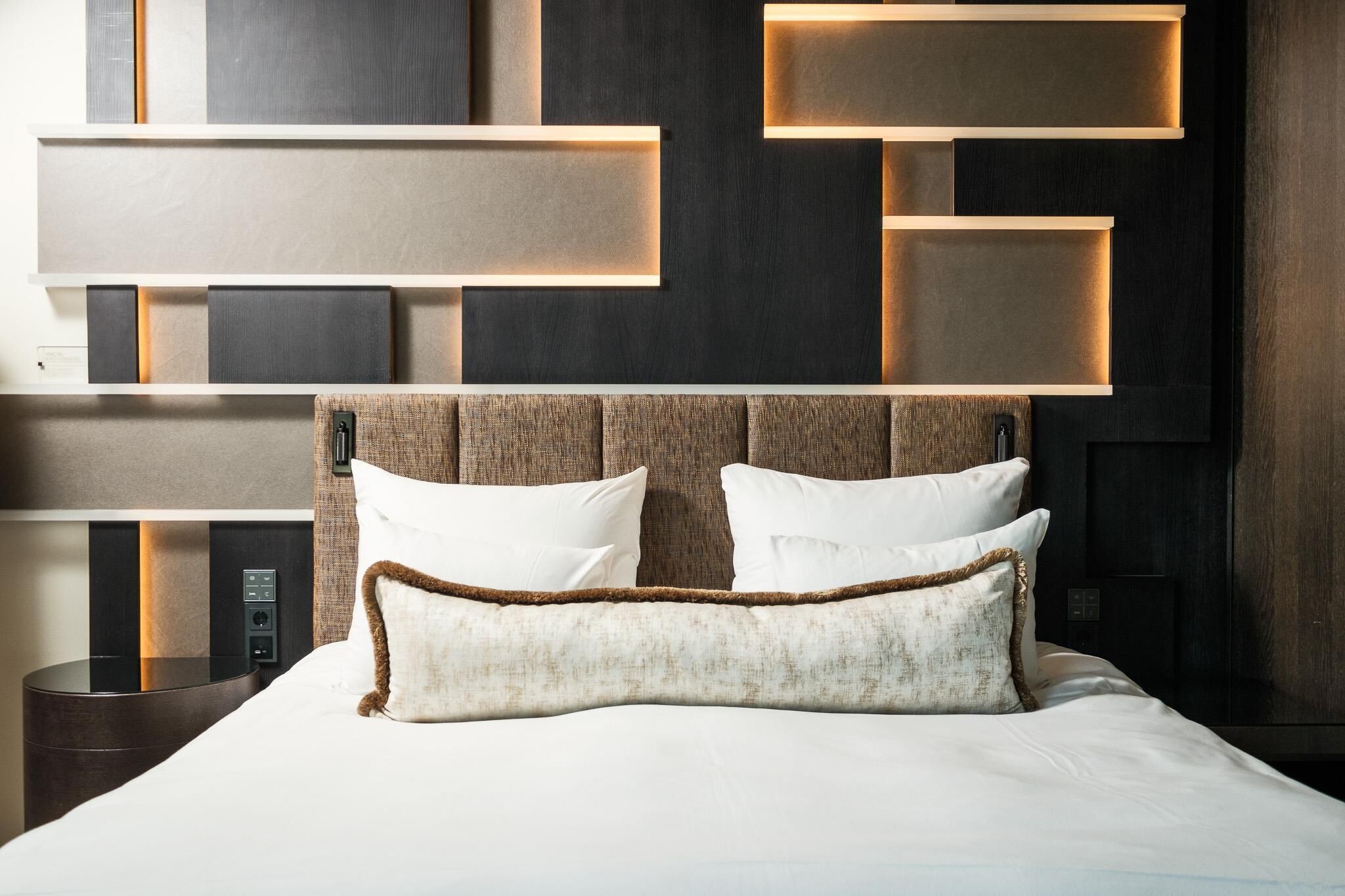 Una habitación de hotel moderna con una cama grande, un cabecero con iluminación integrada y un panel de control en la pared.