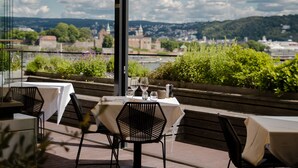 An outdoor dining area with tables and chairs, overlooking a scenic view of a town and hills.