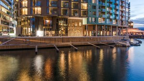 A modern hotel with a waterfront view, featuring a curved facade, multiple balconies, and a dock with boats.